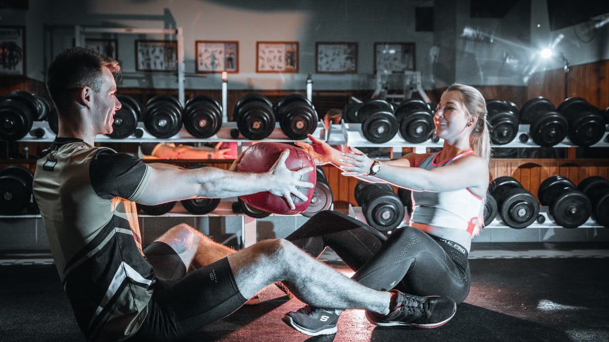 A couple engaged in a fitness session using a medicine ball in a gym environment.